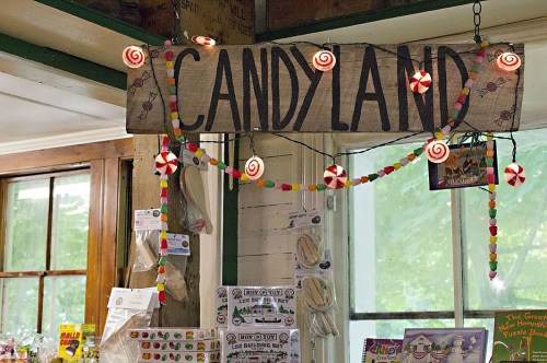 A wooden sign reading "Candyland" adorned with colorful decorations and candy-themed ornaments in a shop setting.