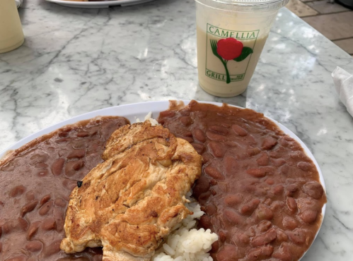 A plate with rice and beans topped with an omelet, alongside a drink in a cup with a rose logo.
