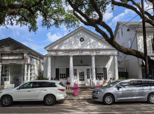 A white building with columns, labeled "Camellia Grill," surrounded by trees and parked cars on a sunny day.