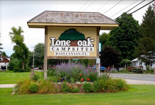 Sign for Lone Oak Campsites in East Canaan, CT, surrounded by greenery and colorful flowers.