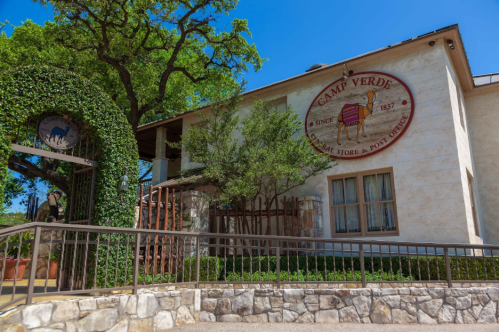 Exterior view of Camp Verde, a historic store and post office, featuring greenery and a stone wall.