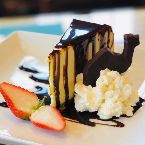 A slice of layered chocolate cake with whipped cream, chocolate drizzle, and a strawberry on a white plate.