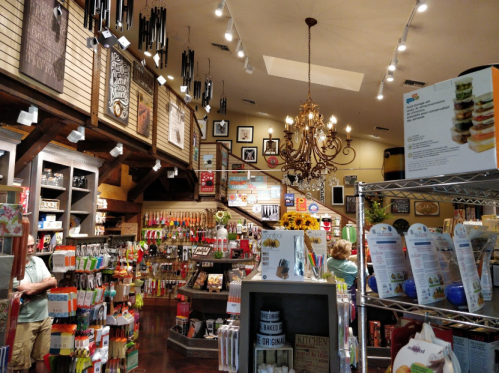A cozy store interior filled with colorful kitchenware, decor, and a chandelier, with customers browsing.