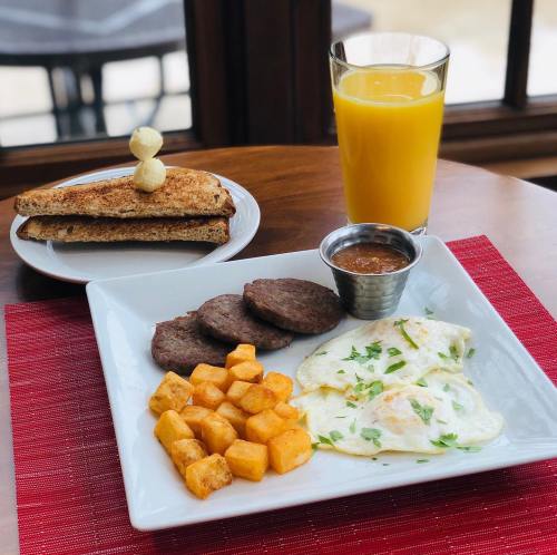 A breakfast plate with eggs, sausage, diced potatoes, toast, and a glass of orange juice on a wooden table.