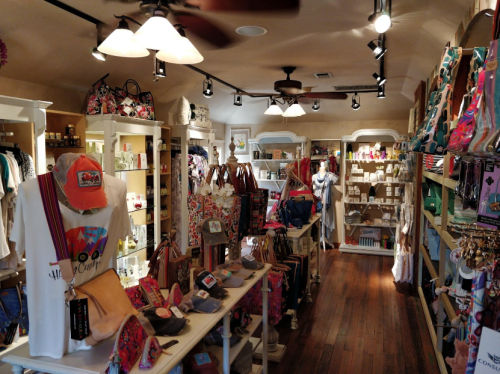 A cozy retail store interior filled with bags, clothing, and accessories displayed on shelves and tables.