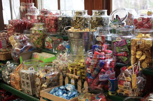 A colorful display of various candies and treats in glass jars on a wooden table, creating a nostalgic candy shop atmosphere.