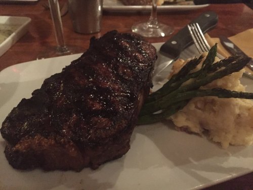 A juicy steak on a plate, accompanied by mashed potatoes and asparagus, set on a wooden table.