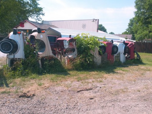 Abandoned cars overgrown with plants, lined up in a grassy area near a building.