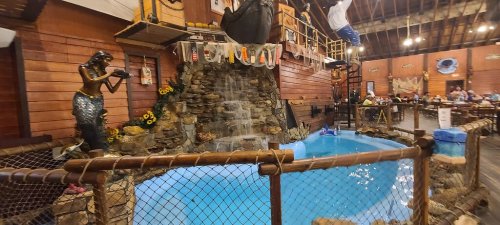 Indoor setting featuring a small pool with a waterfall, surrounded by rustic decor and a mermaid statue.