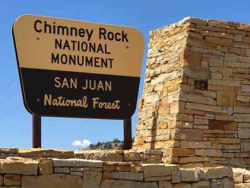 Sign for Chimney Rock National Monument in San Juan National Forest, featuring stone structure and blue sky.