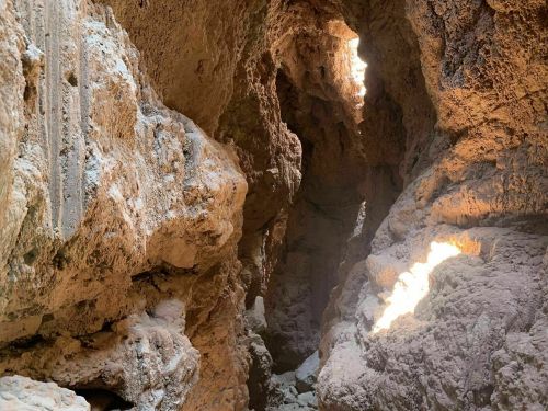 A narrow canyon with rugged rock walls and sunlight streaming through openings above.