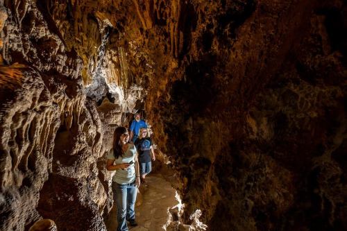 Three people explore a dimly lit cave with rocky walls and formations.