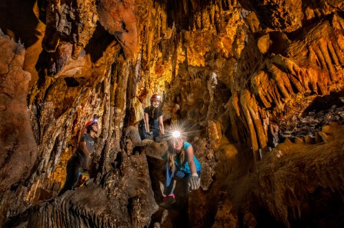 A group of four people exploring a cave, surrounded by stunning rock formations and illuminated by headlamps.