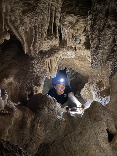 A person with a headlamp explores a narrow cave, surrounded by unique rock formations.