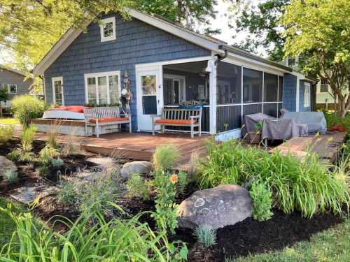 A charming blue house with a porch, surrounded by lush greenery and landscaped rocks.