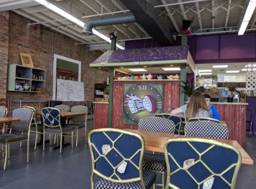 A cozy café interior with colorful decor, wooden tables, and chairs, featuring a counter with a whimsical design.