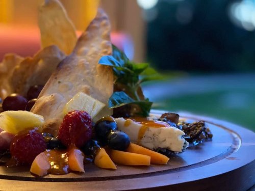 A beautifully arranged platter featuring fruits, cheese, and crispy elements, set against a blurred outdoor background.