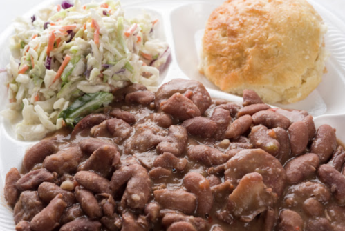 A plate with seasoned pinto beans, coleslaw, and a biscuit.