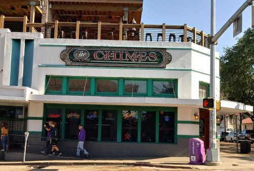 Exterior of a building with a sign reading "The Chimes," featuring large windows and a second-floor patio.