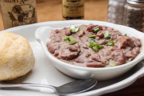 A bowl of red beans topped with green onions, served with a biscuit on a plate, with condiments in the background.