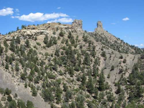 Rocky hills with sparse vegetation under a blue sky, featuring two prominent rock formations.