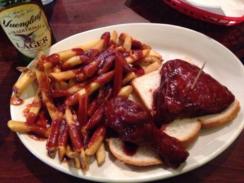 A plate with BBQ chicken, two slices of bread, fries, and a bottle of lager.