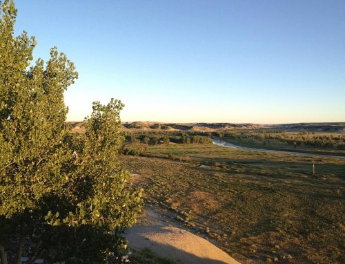 A serene landscape featuring rolling hills, a winding river, and green vegetation under a clear blue sky.
