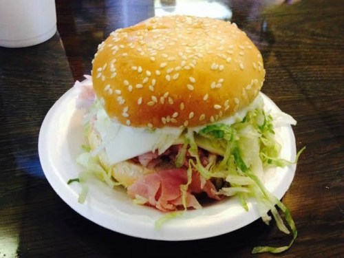 A sesame seed bun sandwich filled with lettuce and layers of meat on a white plate.