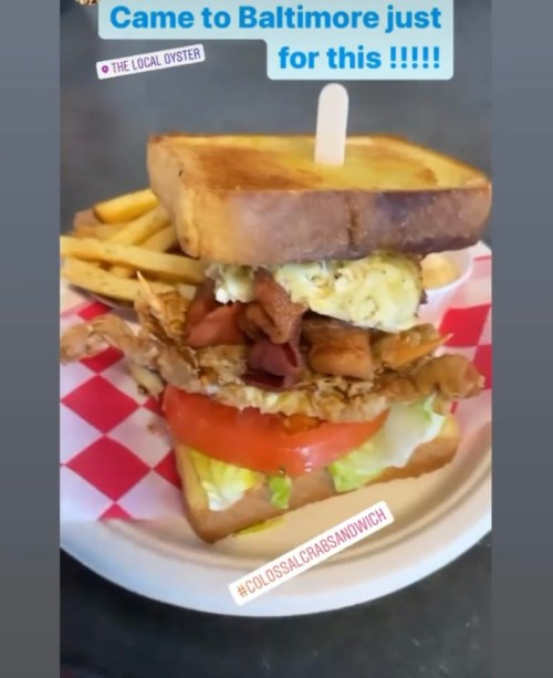 A towering sandwich with crab, bacon, lettuce, and tomato, served with fries on a plate.