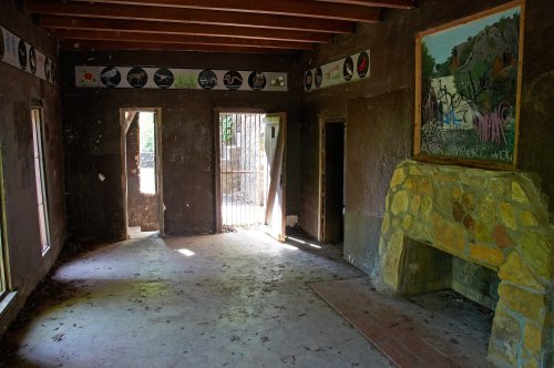Abandoned room with a stone fireplace, graffiti on the walls, and two open doorways, illuminated by natural light.