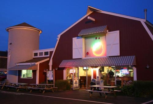 A red barn-style building with a neon sign, picnic tables outside, and a silo in the background, illuminated at dusk.