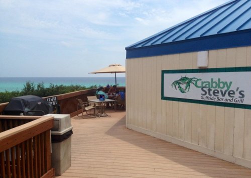 View of Crabby Steve's Gulfsid Bar and Grill with a deck overlooking the ocean and a grill in the foreground.