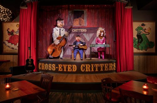 A stage with animatronic animals performing music, surrounded by red curtains and rustic decor in a lively setting.