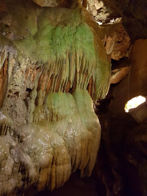 Stalactites and rock formations in a cave, featuring green hues and intricate textures.