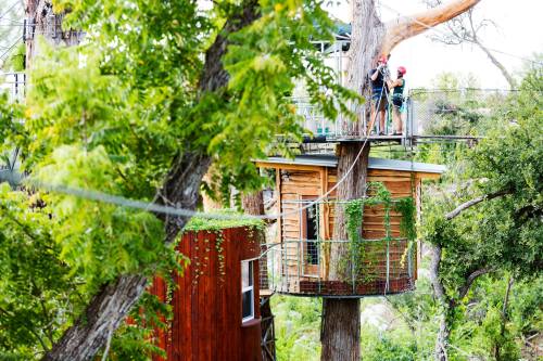 A treehouse surrounded by greenery, with two people preparing for an adventure on a zip line.