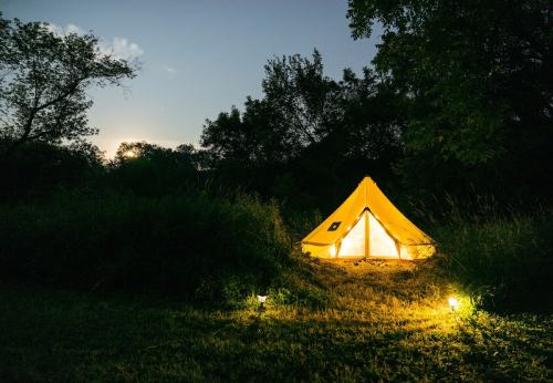 A glowing yellow tent in a grassy area at dusk, surrounded by trees and soft lighting.