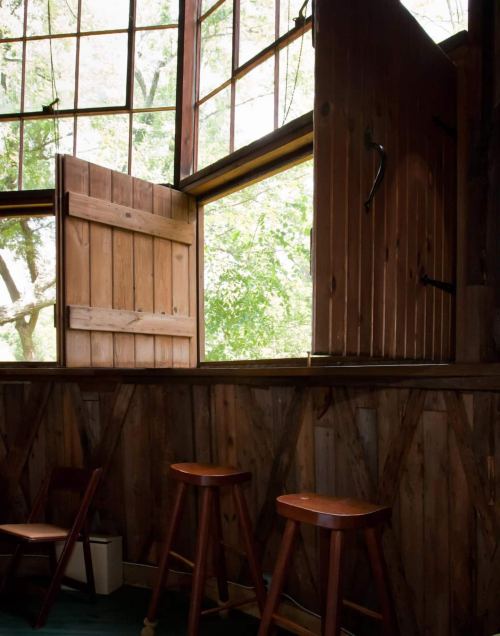 Open wooden windows in a rustic room, with two wooden stools and greenery visible outside.
