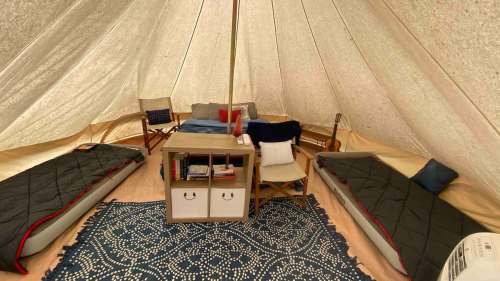 Cozy interior of a tent with two beds, a small table, and seating, decorated with a blue rug.