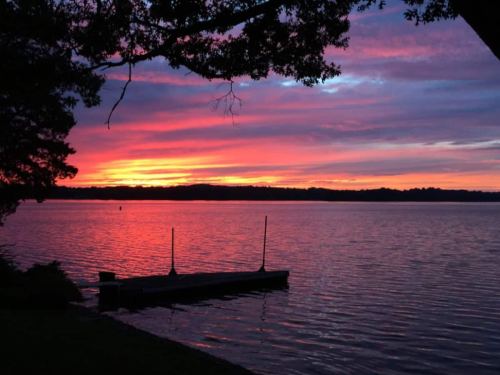 A serene lake at sunset, with vibrant pink and orange skies reflecting on the water and a small dock in the foreground.