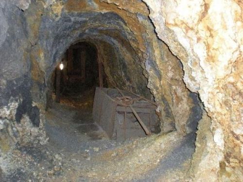A dimly lit mine tunnel with rough stone walls and an old wooden cart on the ground.