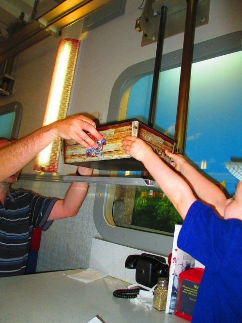 A child's hand reaches for a wooden box being passed from an adult in a diner setting.