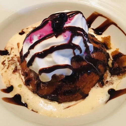 A warm dessert topped with whipped cream, chocolate drizzle, and a berry, served on a creamy sauce.