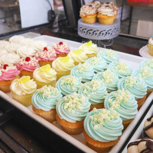 A display of colorful cupcakes with various frosting designs, including pink, yellow, and blue, arranged on a tray.