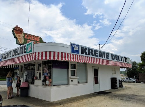 A small ice cream shop with a striped awning, featuring a sign that reads "Kreme Delite" and a vintage ice cream cone.