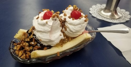 A banana split topped with whipped cream, cherries, and chopped nuts, served in a glass dish.