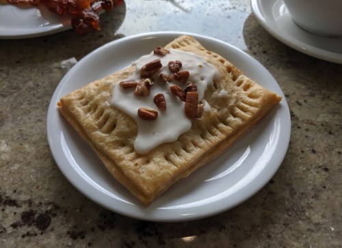 A pastry topped with white icing and chopped nuts on a small white plate.