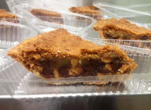 A slice of chocolate chip cookie pie in a clear plastic container, showcasing its golden-brown crust and chocolate chips.
