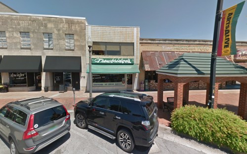 A street view of a small town with shops, parked cars, and a gazebo in the foreground.