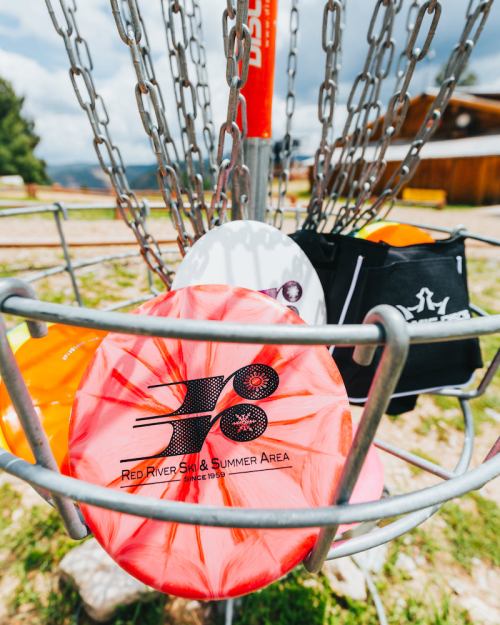 A close-up of a disc golf basket with colorful discs, set against a scenic outdoor background.