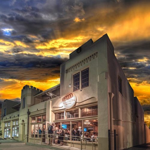 A building with large windows under a dramatic sunset sky, casting warm colors over the scene.